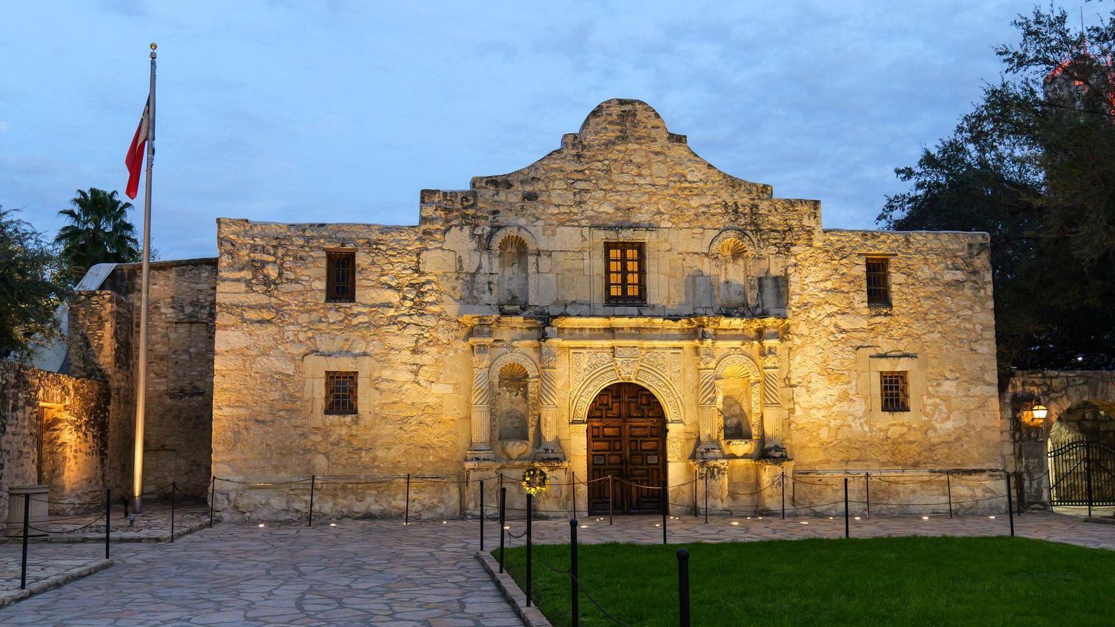 The Alamo lit at dusk beneath the Texas flag in San Antonio