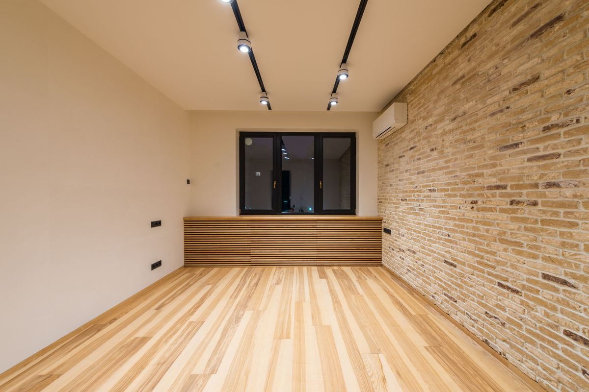 Empty room with a brick wall, wood floor and a window bench