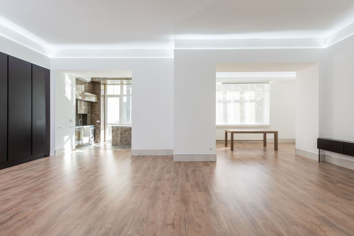 Empty apartment rooms with wood floors and a dining table beyond