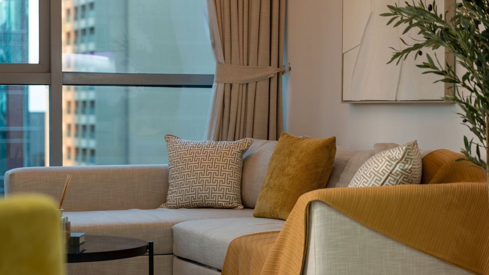 Sofa with cushions and a folded throw beside a city window